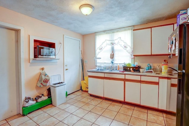 kitchen featuring a textured ceiling, light tile patterned flooring, white cabinetry, light countertops, and black fridge