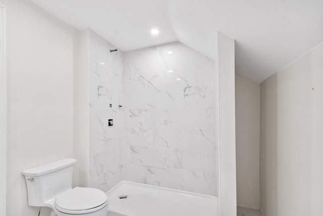 bathroom featuring toilet, a tile shower, and vaulted ceiling