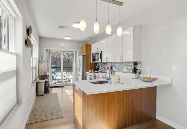 kitchen featuring visible vents, light countertops, a peninsula, stainless steel appliances, and backsplash