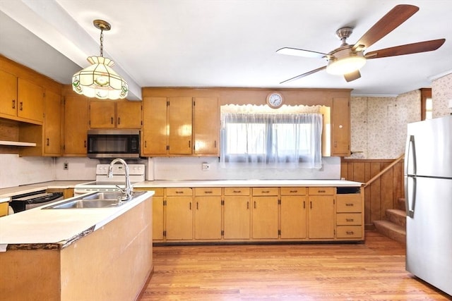 kitchen with light hardwood / wood-style flooring, stainless steel appliances, hanging light fixtures, ceiling fan, and a center island with sink