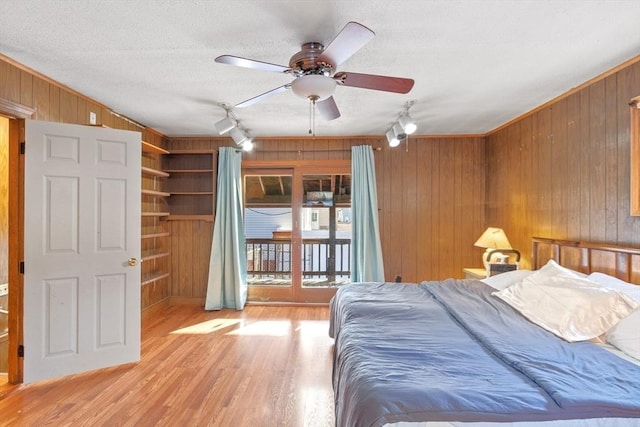 bedroom featuring ceiling fan, a textured ceiling, rail lighting, light hardwood / wood-style floors, and wooden walls