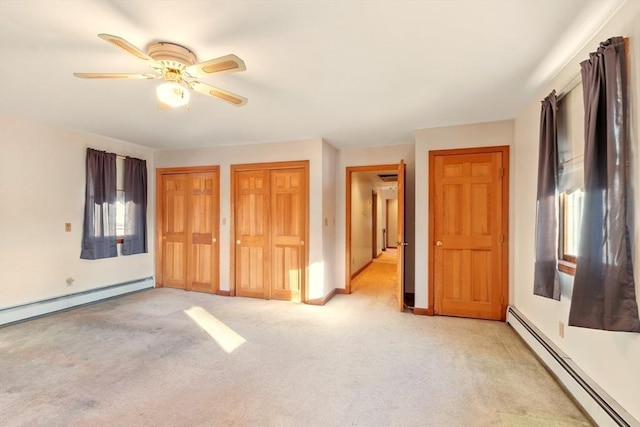 unfurnished bedroom with ceiling fan, multiple closets, light carpet, and a baseboard heating unit