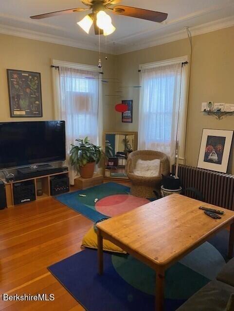 living room featuring wood-type flooring, ornamental molding, and ceiling fan