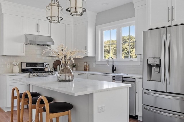 kitchen featuring sink, stainless steel appliances, extractor fan, decorative light fixtures, and a kitchen island