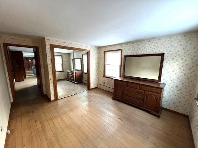 unfurnished bedroom featuring multiple windows, a baseboard heating unit, a closet, and light wood-type flooring