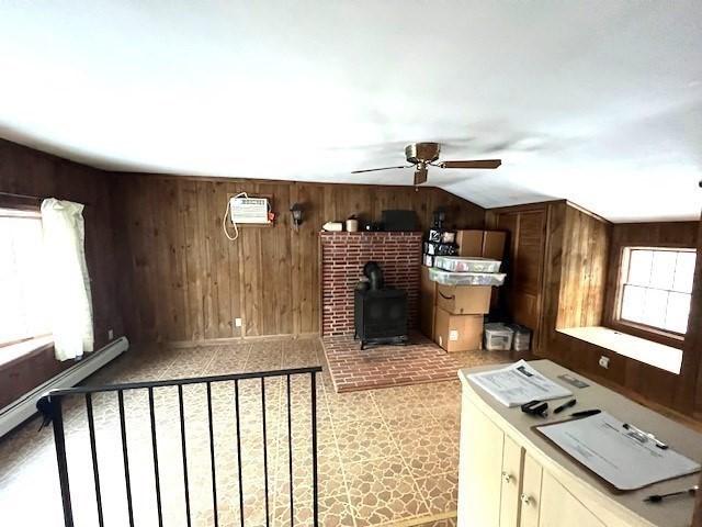 kitchen featuring lofted ceiling, a wood stove, wooden walls, ceiling fan, and cream cabinets