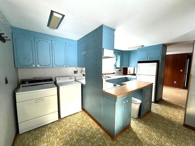 kitchen with washing machine and dryer, white fridge, and blue cabinetry