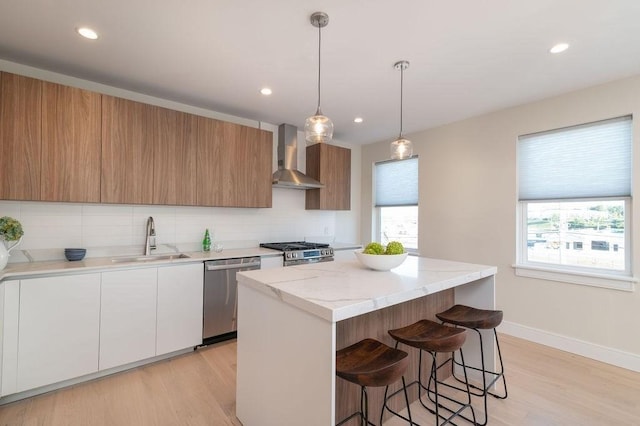 kitchen with stainless steel appliances, a sink, a center island, wall chimney exhaust hood, and tasteful backsplash