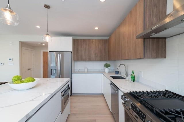 kitchen featuring modern cabinets, appliances with stainless steel finishes, light stone countertops, ventilation hood, and a sink