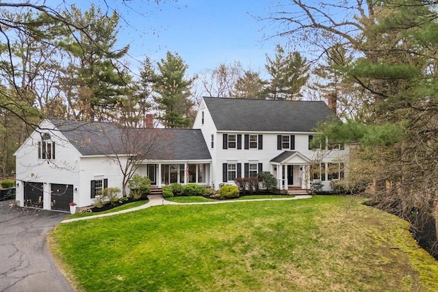 colonial house with a garage, a chimney, a front lawn, and aphalt driveway