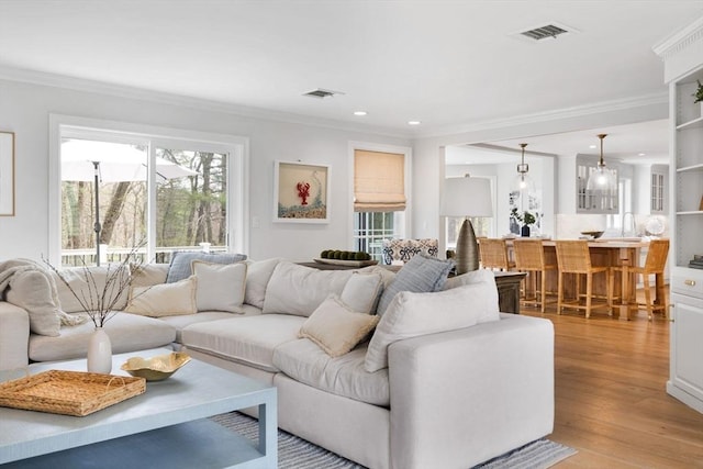 living area with recessed lighting, visible vents, ornamental molding, and light wood-style flooring