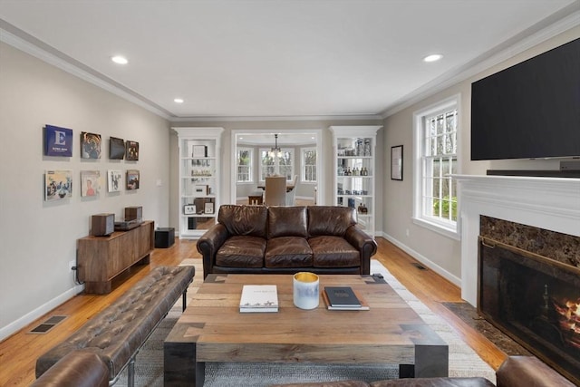 living area with visible vents, crown molding, baseboards, light wood-type flooring, and a premium fireplace