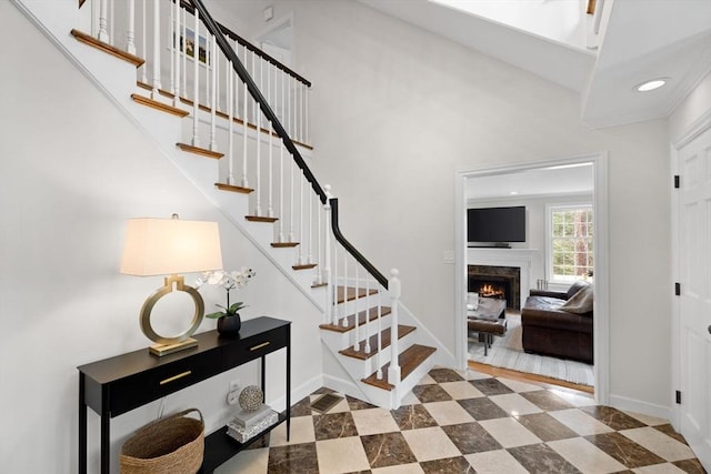 stairway featuring baseboards, recessed lighting, a high ceiling, and a premium fireplace