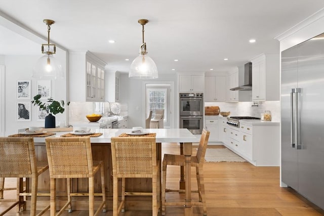 kitchen featuring decorative backsplash, a kitchen breakfast bar, appliances with stainless steel finishes, white cabinets, and wall chimney exhaust hood