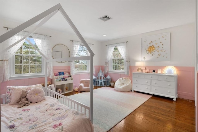 bedroom with visible vents, wainscoting, and wood finished floors