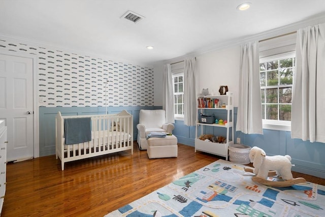 bedroom with crown molding, a nursery area, visible vents, and wood finished floors