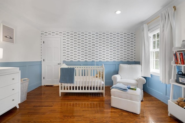 bedroom with crown molding, wainscoting, a decorative wall, wood finished floors, and a crib