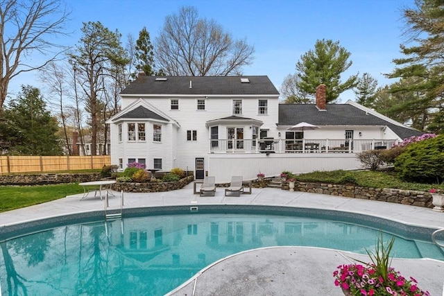rear view of property with fence, a wooden deck, a fenced in pool, a chimney, and a patio area