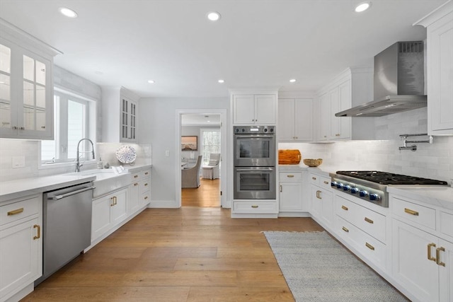 kitchen featuring white cabinets, appliances with stainless steel finishes, plenty of natural light, and wall chimney exhaust hood