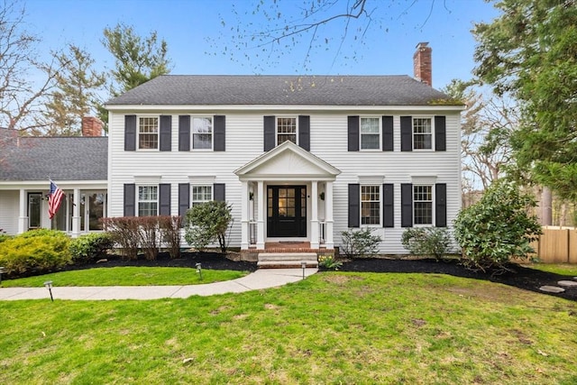 colonial home featuring fence, a chimney, and a front yard