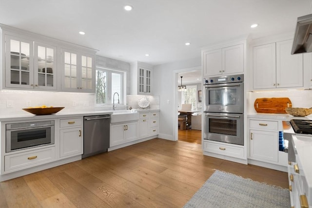kitchen featuring a sink, light wood-style floors, light countertops, stainless steel appliances, and backsplash