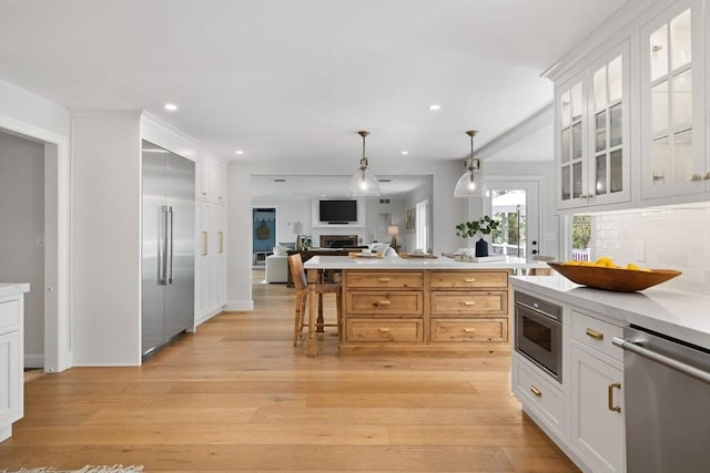 kitchen featuring decorative backsplash, built in appliances, open floor plan, light countertops, and decorative light fixtures