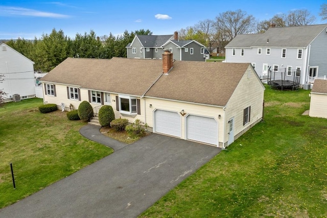 view of front of property featuring a front lawn, aphalt driveway, a chimney, an attached garage, and a trampoline