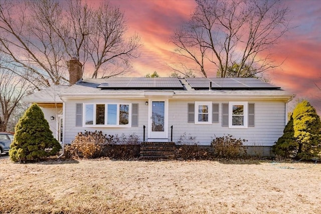 view of front of house with solar panels, entry steps, and a chimney