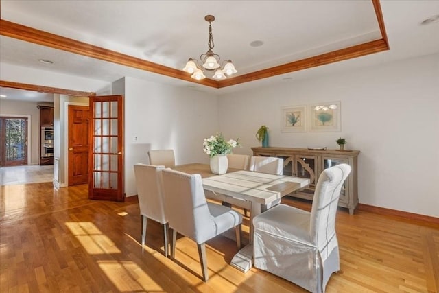 dining room with a raised ceiling, light wood-type flooring, and a chandelier