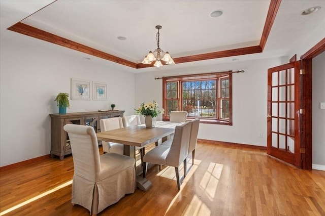 dining area with a tray ceiling, ornamental molding, light hardwood / wood-style floors, and an inviting chandelier