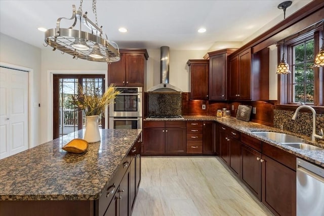 kitchen with wall chimney range hood, sink, decorative backsplash, appliances with stainless steel finishes, and a kitchen island