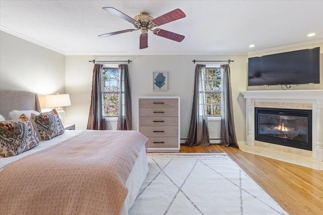 bedroom featuring ornamental molding, ceiling fan, a baseboard radiator, light hardwood / wood-style flooring, and a tiled fireplace