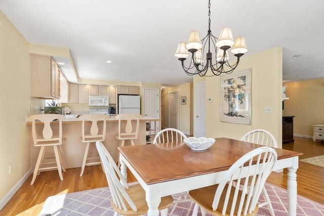 dining space featuring an inviting chandelier, baseboards, and light wood-style flooring