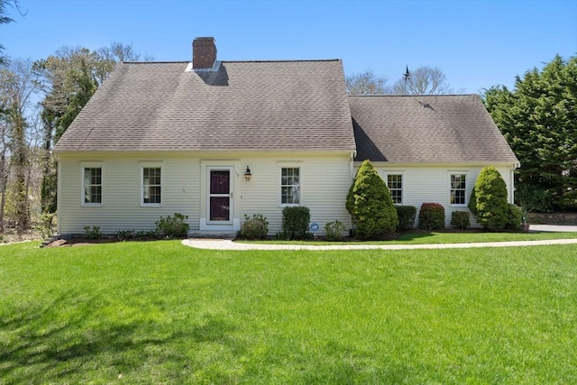 new england style home featuring a chimney, a shingled roof, and a front yard