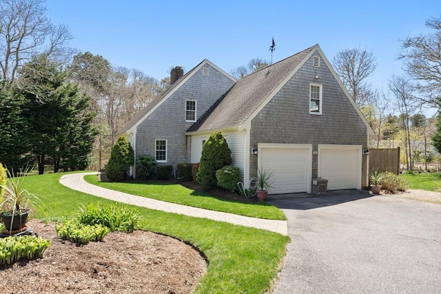 view of front facade with driveway, a chimney, a front yard, and a garage