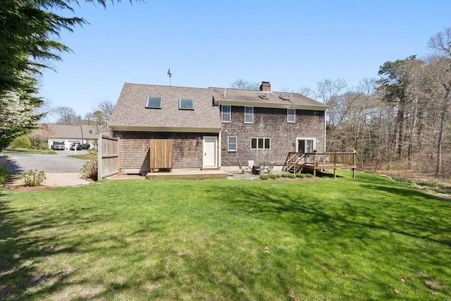 rear view of house featuring a shingled roof, a wooden deck, a yard, and a chimney
