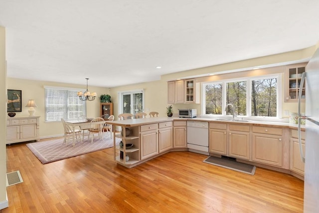 kitchen with a sink, light wood finished floors, white appliances, a peninsula, and visible vents