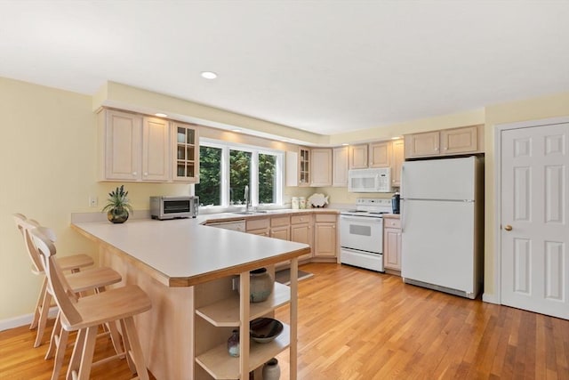 kitchen with light countertops, a peninsula, white appliances, and a breakfast bar