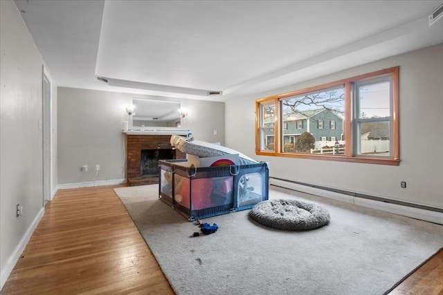 bedroom featuring a tray ceiling, a brick fireplace, a baseboard radiator, and hardwood / wood-style flooring