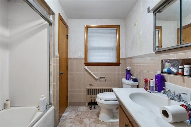 full bathroom with radiator heating unit, toilet, shower / bath combination with glass door, vanity, and tile walls