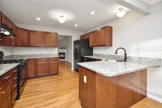 kitchen with black appliances, light hardwood / wood-style floors, light stone countertops, kitchen peninsula, and sink