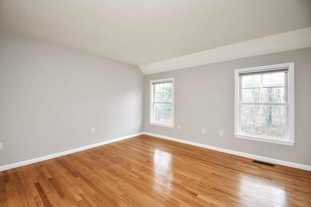 spare room featuring vaulted ceiling, light hardwood / wood-style floors, and a wealth of natural light