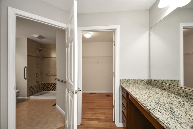 bathroom featuring hardwood / wood-style floors, a tile shower, toilet, and vanity