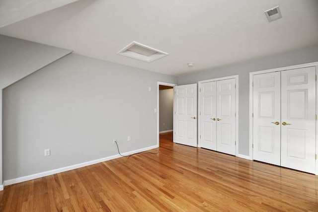 unfurnished bedroom featuring two closets and light hardwood / wood-style floors