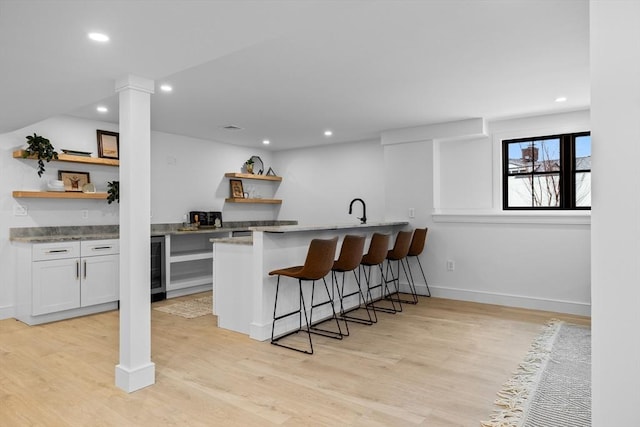 kitchen with open shelves, light wood-style floors, a breakfast bar area, and recessed lighting