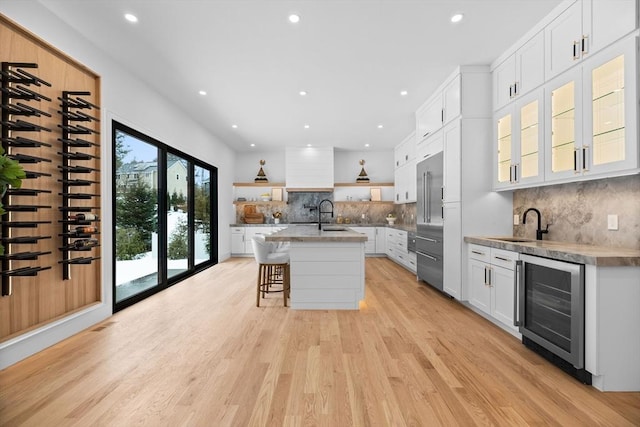 kitchen featuring open shelves, beverage cooler, light wood finished floors, and a sink