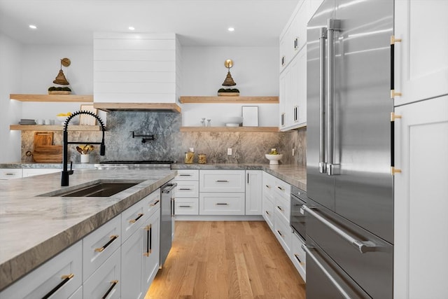 kitchen featuring open shelves, light wood-type flooring, appliances with stainless steel finishes, white cabinetry, and a sink