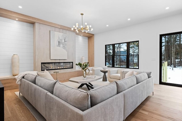 living area with a glass covered fireplace, recessed lighting, light wood-type flooring, and an inviting chandelier