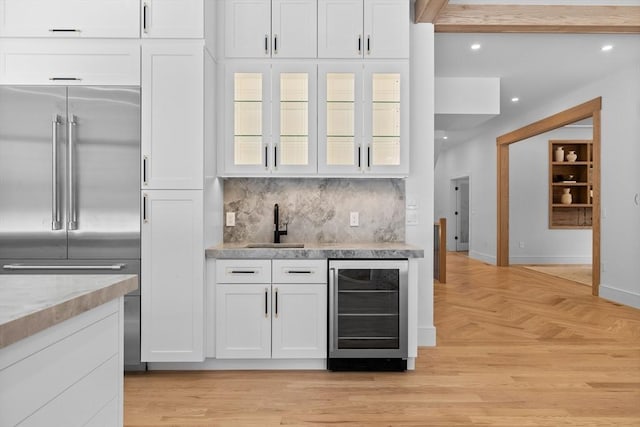 kitchen with beverage cooler, a sink, tasteful backsplash, built in fridge, and white cabinetry