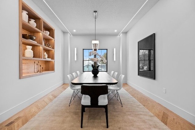 dining area featuring visible vents, baseboards, a textured ceiling, and light wood-style flooring